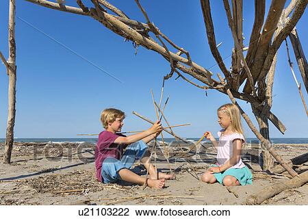 Stock Image - Boy and his sister constructing a circular structure from driftwood, Caleri Beach, Veneto, Italy. Fotosearch