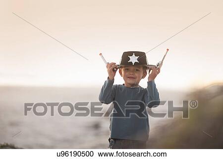 Boy dressed as cowboy sheriff holding onto hat and toy guns in sand dunes View Large Photo Image Stock Image - Boy dressed as cowboy sheriff holding onto hat and toy guns in sand dunes. Fotosearch