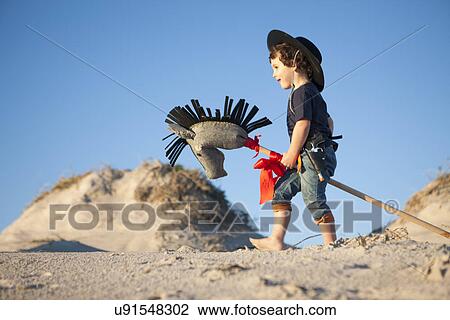 Stock Image - Boy dressed as cowboy with hobby horse in sand dunes. Fotosearch