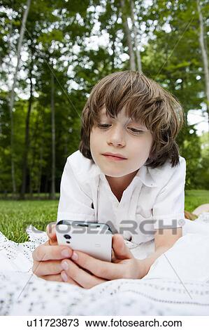 Boy lying on front reading messages on smartphone View Large Photo Image Stock Image - Boy lying on front reading messages on smartphone. Fotosearch