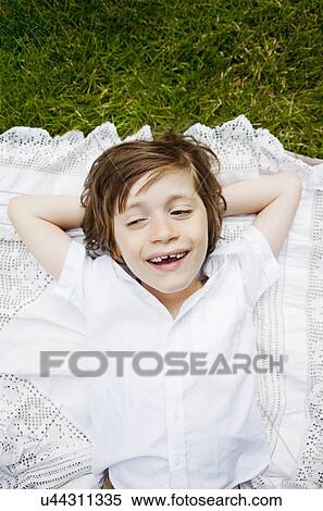 Stock Photography - Boy lying on tablecloth on grass with hands behind head. Fotosearch