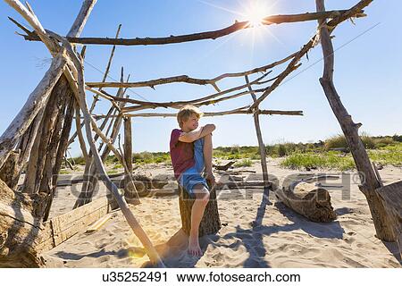 Stock Image - Boy making a break in driftwood shelter, Caleri Beach, Veneto, Italy. Fotosearch
