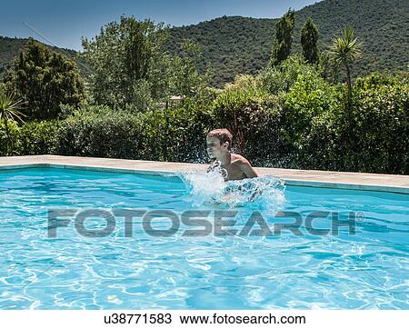 Stock Image - Boy splashing and playing in swimming pool, Capoterra, Sardinia, Italy. Fotosearch