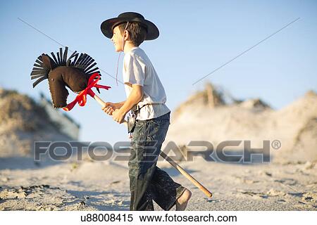 Stock Photography - Boy with hobby horse dressed as cowboy in sand dunes. Fotosearch