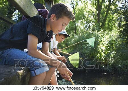 Stock Photo - Boys sitting on bridge, fishing. Fotosearch