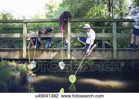 Stock Image - Boys using fishing nets on bridge. Fotosearch