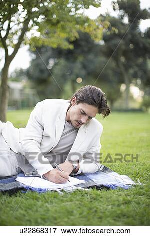 Businessman reclining on picnic blanket writing notes in park View Large Photo Image Stock Photo - Businessman reclining on picnic blanket writing notes in park. Fotosearch