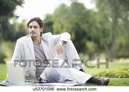 Businessman reclining on picnic blanket using laptop in park View Large Photo Image Stock Photograph - Businessman reclining on picnic blanket using laptop in park. Fotosearch
