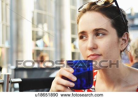 Stock Image - Close up of young woman having a drink at sidewalk cafe. Fotosearch