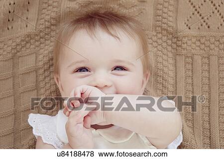 Stock Photo - Close up portrait of smiling baby girl lying on blanket. Fotosearch