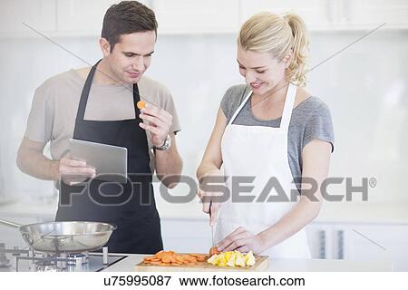 Couple chopping and tasting sliced vegetables in kitchen View Large Photo Image Stock Photo - Couple chopping and tasting sliced vegetables in kitchen. Fotosearch