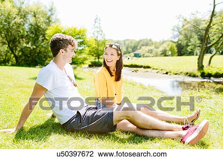 Stock Image - Couple sitting on grass in the park. Fotosearch