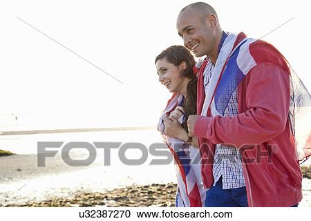 Stock Image - Couple wrapped in british flag strolling on Bournemouth beach, Dorset, UK. Fotosearch