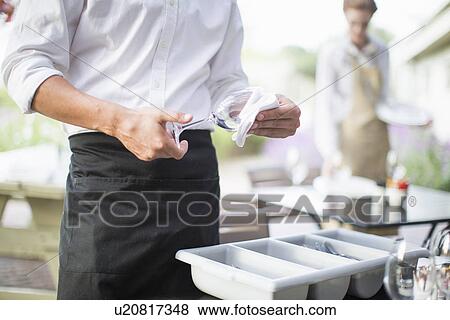 Stock Photo - Cropped shot of waiter polishing wine glasses with napkin in patio restaurant. Fotosearch