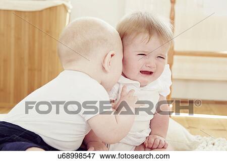 Stock Photo - Crying baby girl with baby boy leaning toward her. Fotosearch