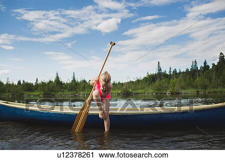 Stock Image - Curious girl looking down at water in Indian river, Ontario, Canada. Fotosearch