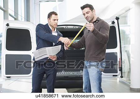 Stock Image - Customer and salesman checking van measurements in car dealership. Fotosearch