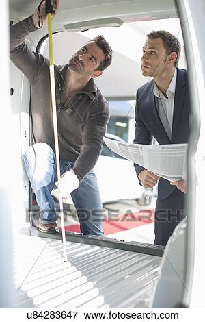 Stock Photo - Customer and salesman checking vehicle interior height in car dealership. Fotosearch