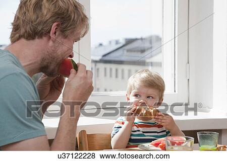 Father and toddler son eating breakfast at kitchen table View Large Photo Image Stock Photo - Father and toddler son eating breakfast at kitchen table. Fotosearch