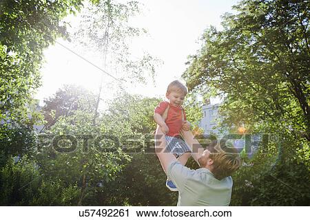 Stock Image - Father holding up toddler son in park. Fotosearch