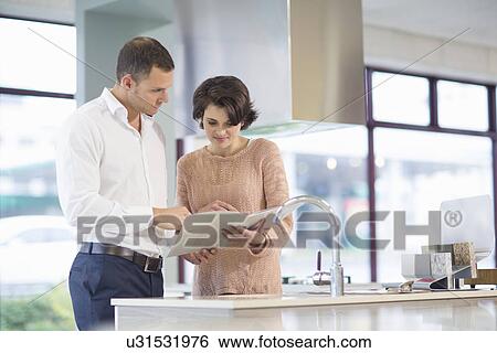 Stock Photograph - Female customer and salesman looking at brochure in kitchen showroom. Fotosearch