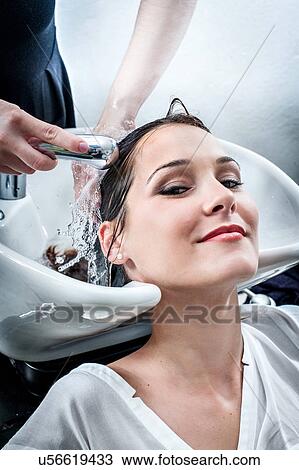Stock Image - Female hairdresser washing young woman's hair in hair salon. Fotosearch