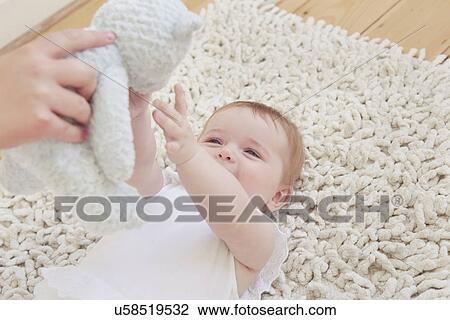 Female hand holding up teddy bear for baby girl lying on rug View Large Photo Image Stock Image - Female hand holding up teddy bear for baby girl lying on rug. Fotosearch
