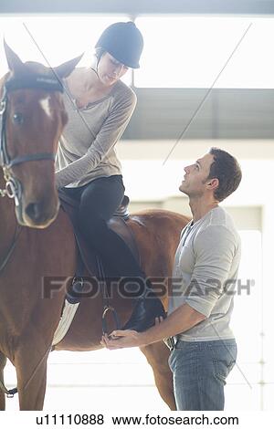 Stock Photo - Female horseback rider with instructor in indoor paddock. Fotosearch