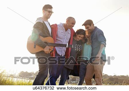 Stock Image - Five adult friends with acoustic guitar on Bournemouth beach, Dorset, UK. Fotosearch