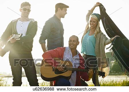 Stock Photo - Four adult friends with acoustic guitar and picnic blanket on Bournemouth beach, Dorset, UK. Fotosearch