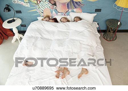 Stock Photography - Four young women friends asleep in hotel bed. Fotosearch