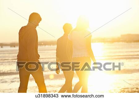 Stock Image - Friends walking on beach at sunset. Fotosearch