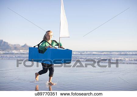 Stock Image - Girl running with toy boat along beach. Fotosearch