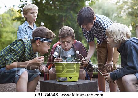 Stock Photograph - Group of young boys toasting marshmallows over bucket barbecue. Fotosearch
