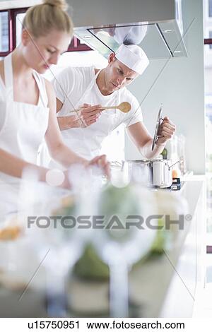 Stock Image - Male and female chefs cooking on hob in commercial kitchen. Fotosearch