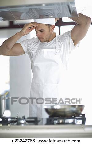 Stock Photograph - Male chef adjusting cap in commercial kitchen. Fotosearch