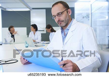 Male doctor looking at records, colleagues having discussion behind View Large Photo Image Stock Image - Male doctor looking at records, colleagues having discussion behind. Fotosearch