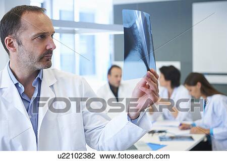 Male doctor looking at x-ray, colleagues having discussion behind View Large Photo Image Stock Image - Male doctor looking at x-ray, colleagues having discussion behind. Fotosearch