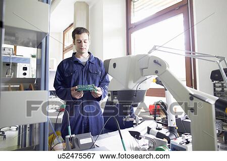 Stock Photo - Male electrician looking down at circuit board in workshop. Fotosearch