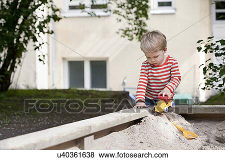 Male toddler pushing toy car in sand pit in garden View Large Photo Image Stock Photo - Male toddler pushing toy car in sand pit in garden. Fotosearch
