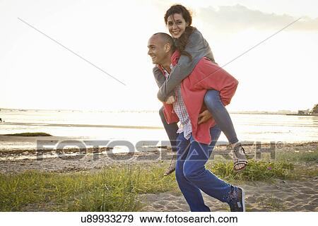 Stock Photo - Man giving piggyback ride to woman on beach. Fotosearch