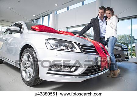 Man looking at new car with red bow with girlfriend in car dealership View Large Photo Image Stock Image - Man looking at new car with red bow with girlfriend in car dealership. Fotosearch