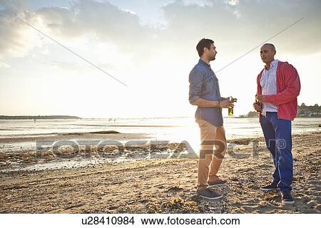 Picture - Men drinking beer and chatting on beach. Fotosearch