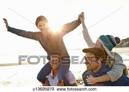 Stock Photo - Men giving piggyback ride to women on beach. Fotosearch