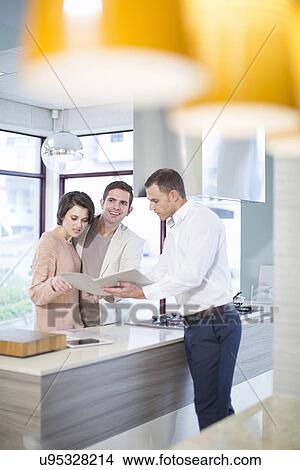 Mid adult couple and salesman looking at brochure in kitchen showroom View Large Photo Image Picture - Mid adult couple and salesman looking at brochure in kitchen showroom. Fotosearch