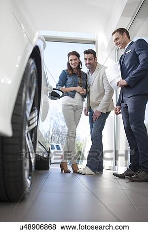 Mid adult couple and salesman looking at car in car dealership View Large Photo Image Stock Photo - Mid adult couple and salesman looking at car in car dealership. Fotosearch