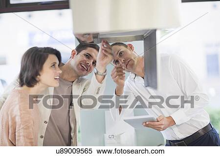 Stock Photography - Mid adult couple and salesman looking at extractor hood in kitchen showroom. Fotosearch