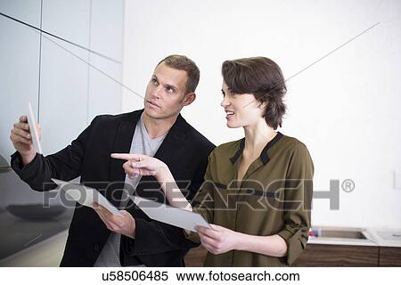 Stock Photography - Mid adult couple choosing ceramic tiles in kitchen showroom. Fotosearch