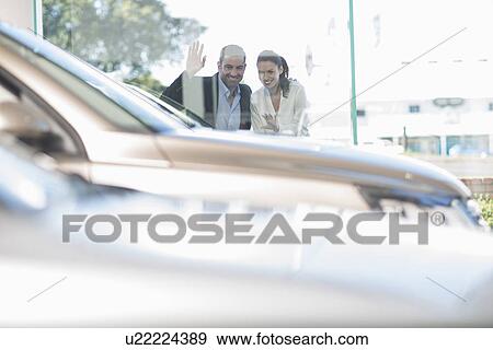 Stock Photo - Mid adult couple looking through car dealership window. Fotosearch