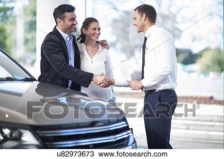 Mid adult couple shaking hands with salesman in car dealership View Large Photo Image Stock Image - Mid adult couple shaking hands with salesman in car dealership. Fotosearch